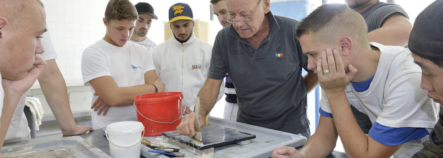 Maler- und Lakierermeister zeigt einer Gruppe von Meisterschülern eine neue Technik.