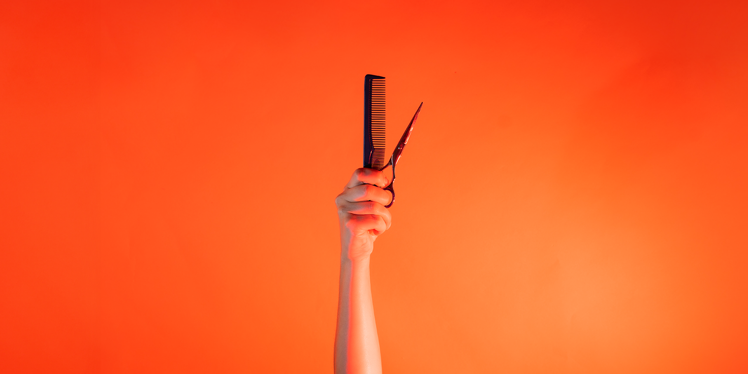 Ein Arm ist vor orangenem Hintergrund senkrecht nach oben gestreckt und hält in der Hand einen Kamm und eine Schere. 