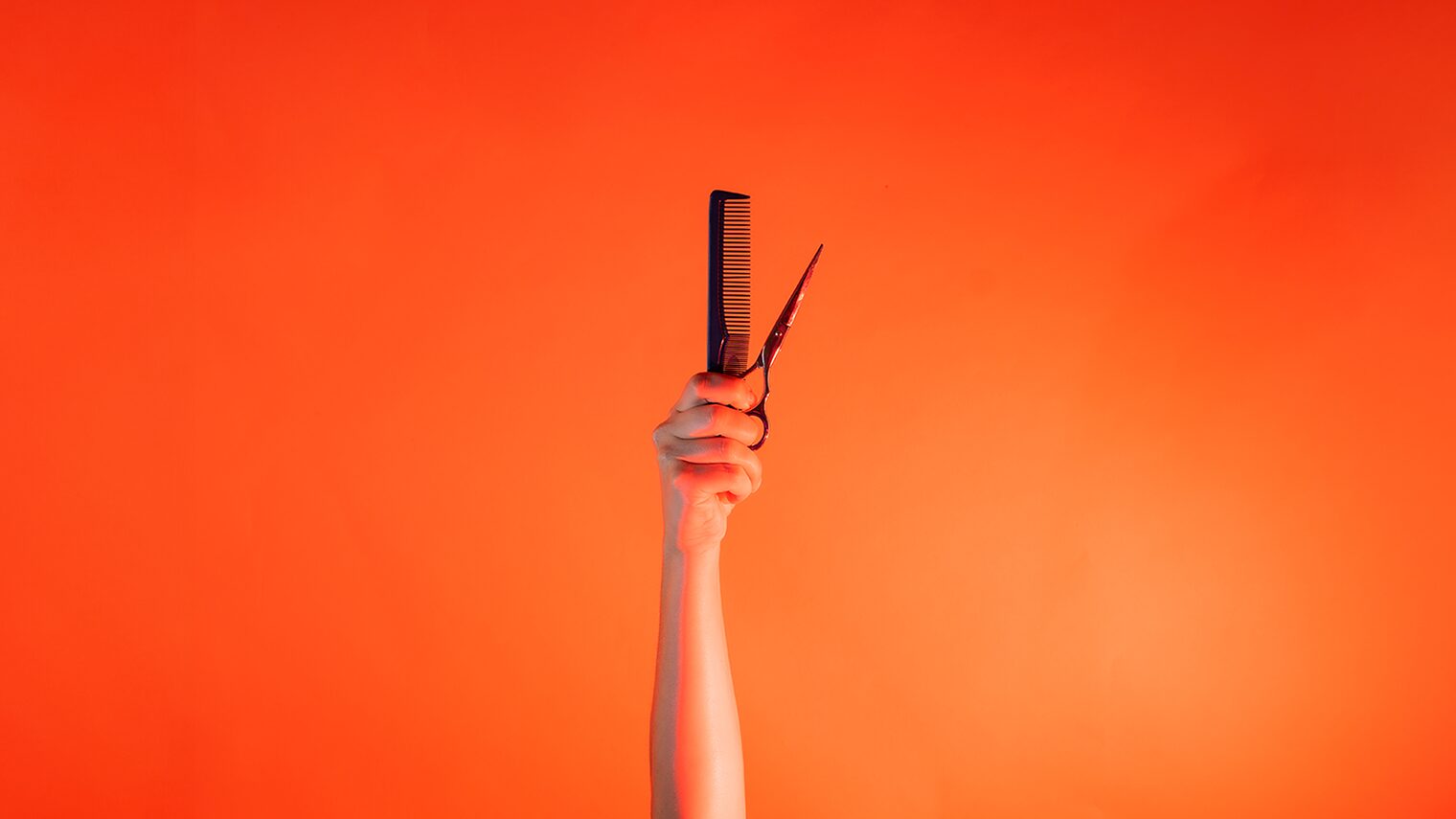 Ein Arm ist vor orangenem Hintergrund senkrecht nach oben gestreckt und hält in der Hand einen Kamm und eine Schere. 