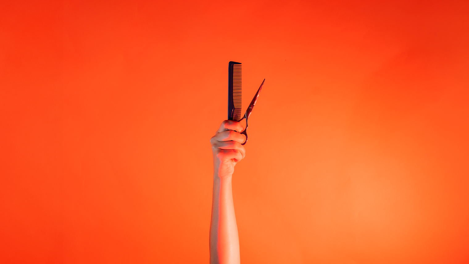 Ein Arm ist vor orangenem Hintergrund senkrecht nach oben gestreckt und hält in der Hand einen Kamm und eine Schere. 