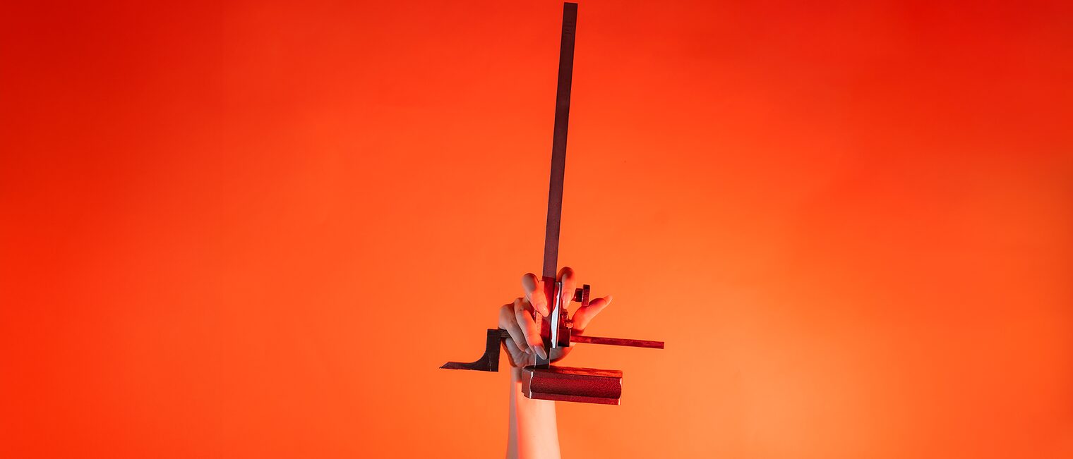 Ein Arm ist vor orangenem Hintergrund senkrecht nach oben gestreckt und in der Hand wird ein Höhenanreißer gehalten.