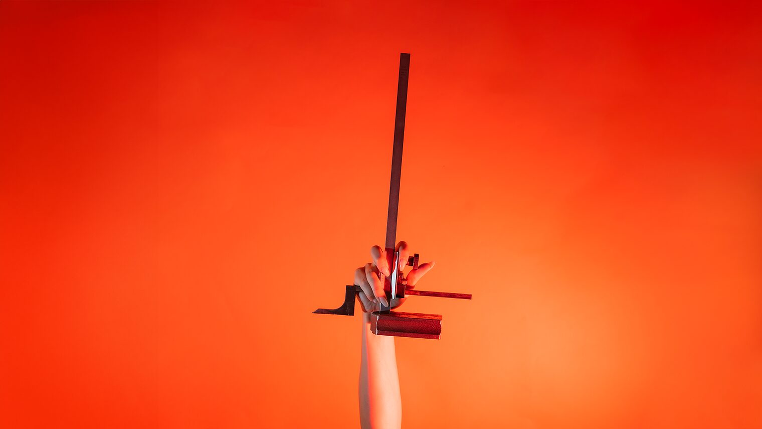 Ein Arm ist vor orangenem Hintergrund senkrecht nach oben gestreckt und in der Hand wird ein Höhenanreißer gehalten.
