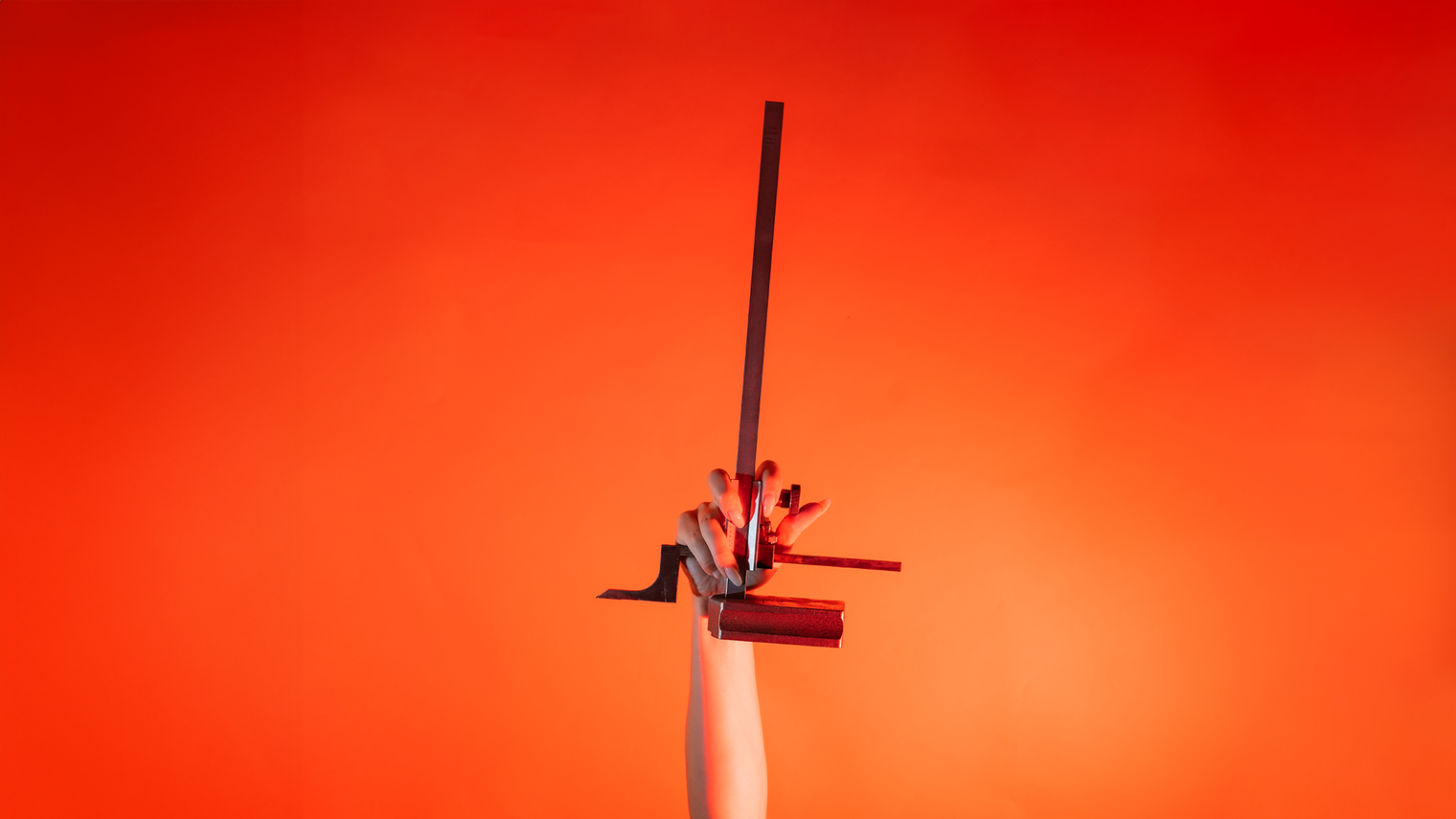 Ein Arm ist vor orangenem Hintergrund senkrecht nach oben gestreckt und in der Hand wird ein Höhenanreißer gehalten.