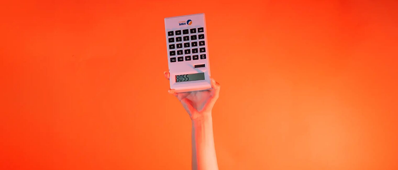Ein Arm ist vor orangenem Hintergrund senkrecht nach oben gestreckt. Die Hand hält einen digitaler Taschenrechner umgedreht.