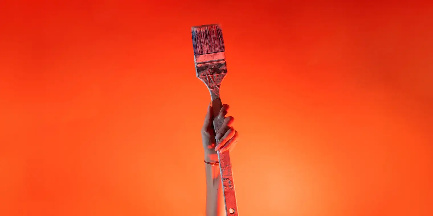 Ein Arm ist vor orangenem Hintergrund senkrecht nach oben gestreckt und in der Hand wird ein Malerpinsel gehalten.