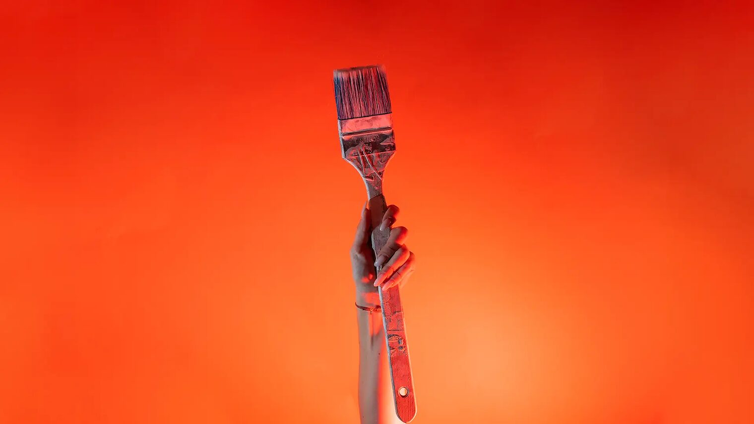 Ein Arm ist vor orangenem Hintergrund senkrecht nach oben gestreckt und in der Hand wird ein Malerpinsel gehalten.