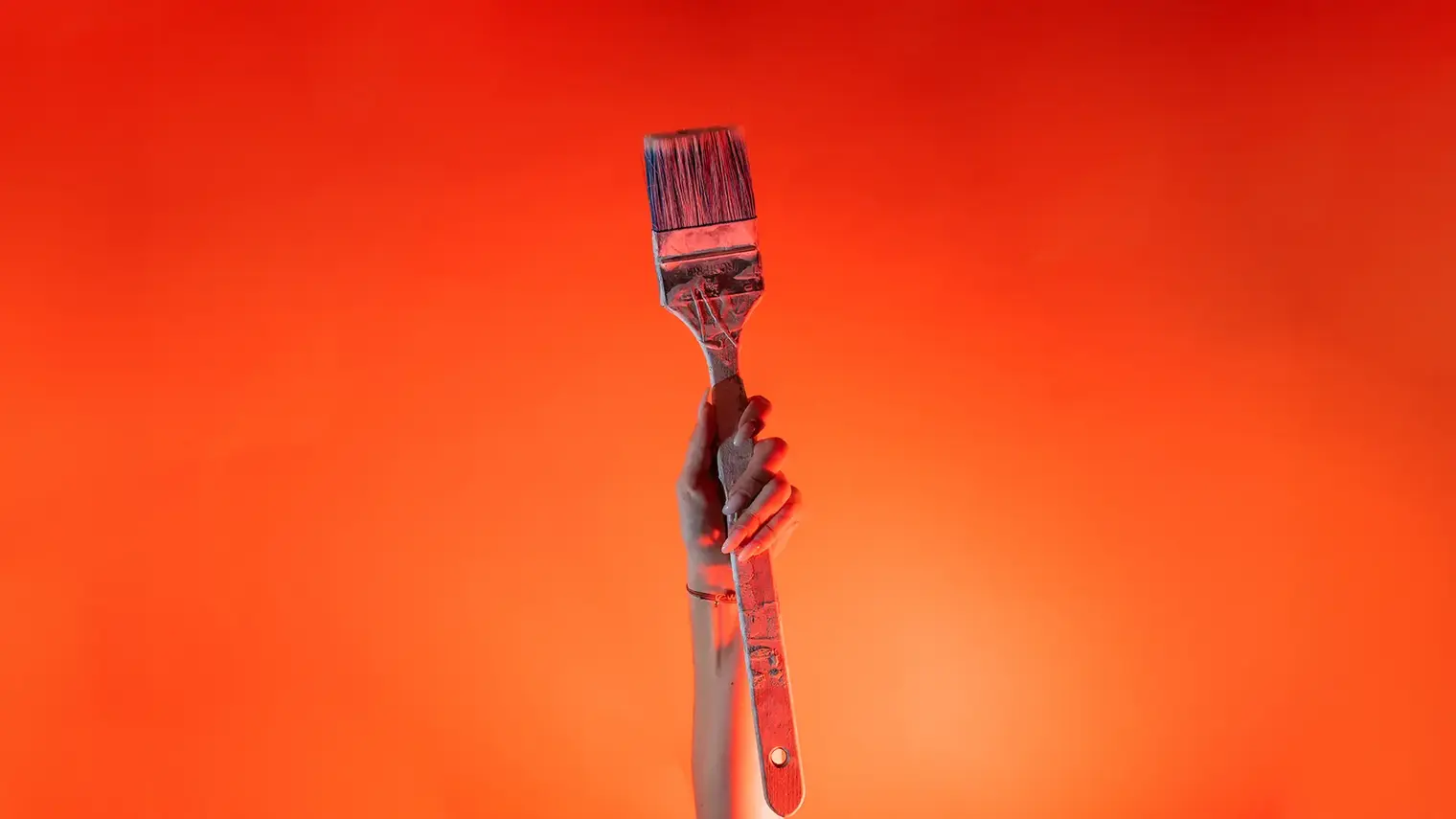 Ein Arm ist vor orangenem Hintergrund senkrecht nach oben gestreckt und in der Hand wird ein Malerpinsel gehalten.