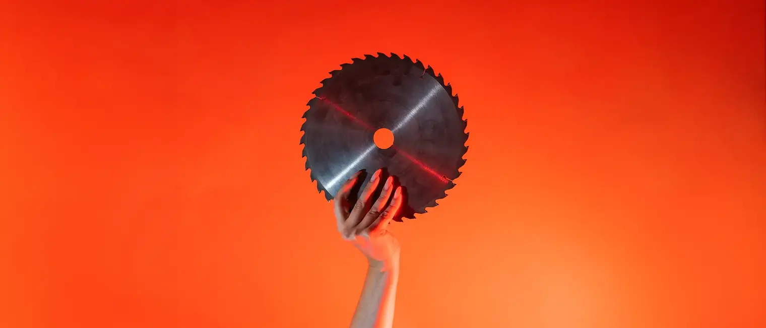 Ein Arm ist vor orangenem Hintergrund senkrecht nach oben gestreckt und in der Hand wird ein rundes Sägeblatt gehalten.