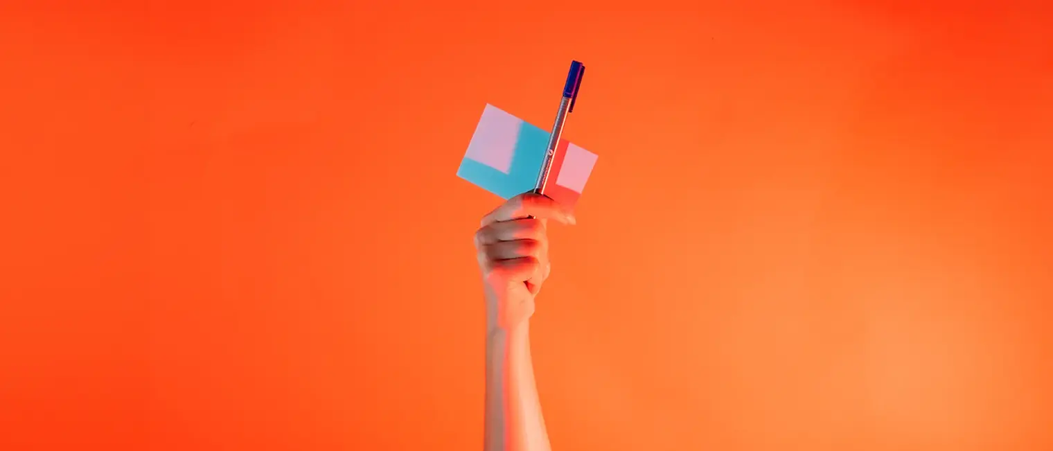 Ein Arm ist vor orangenem Hintergrund senkrecht nach oben gestreckt und hält in der Hand einen Notizblock und eine Stift.