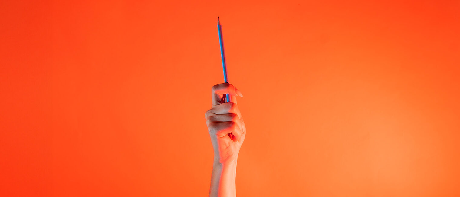 Ein Arm ist vor orangenem Hintergrund senkrecht nach oben gestreckt und hält in der Hand eine Bleistift.