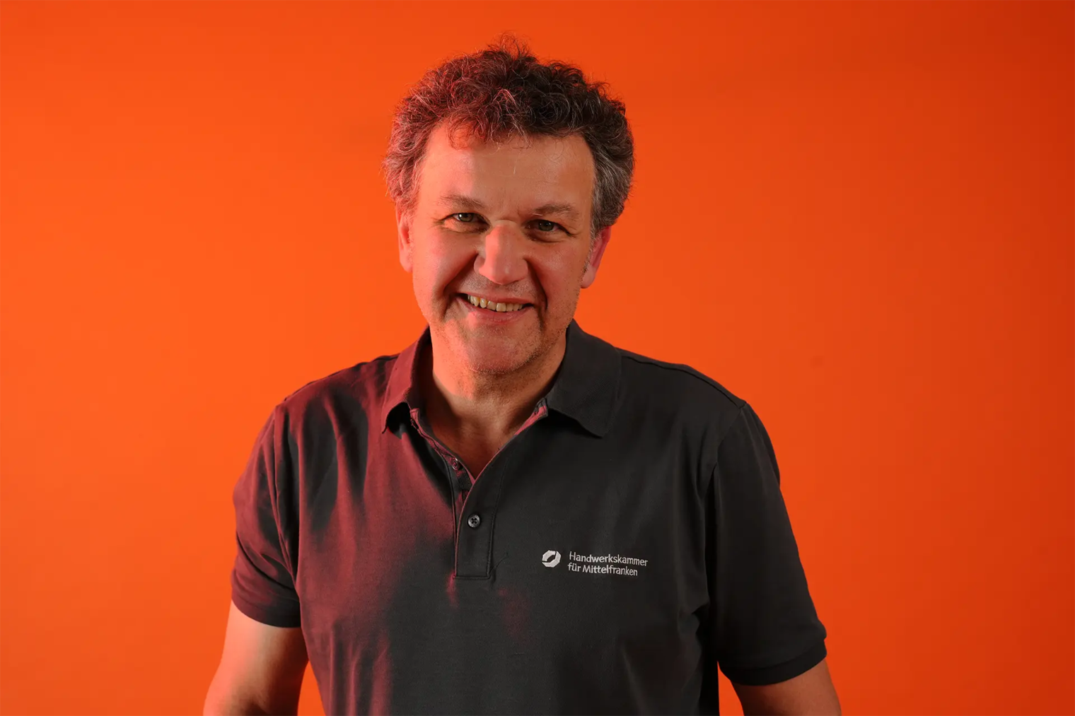 Ein Portrait eines Dozenten, vor orangenem Hintergrund. Herr Lörler, Estrichlegermeister