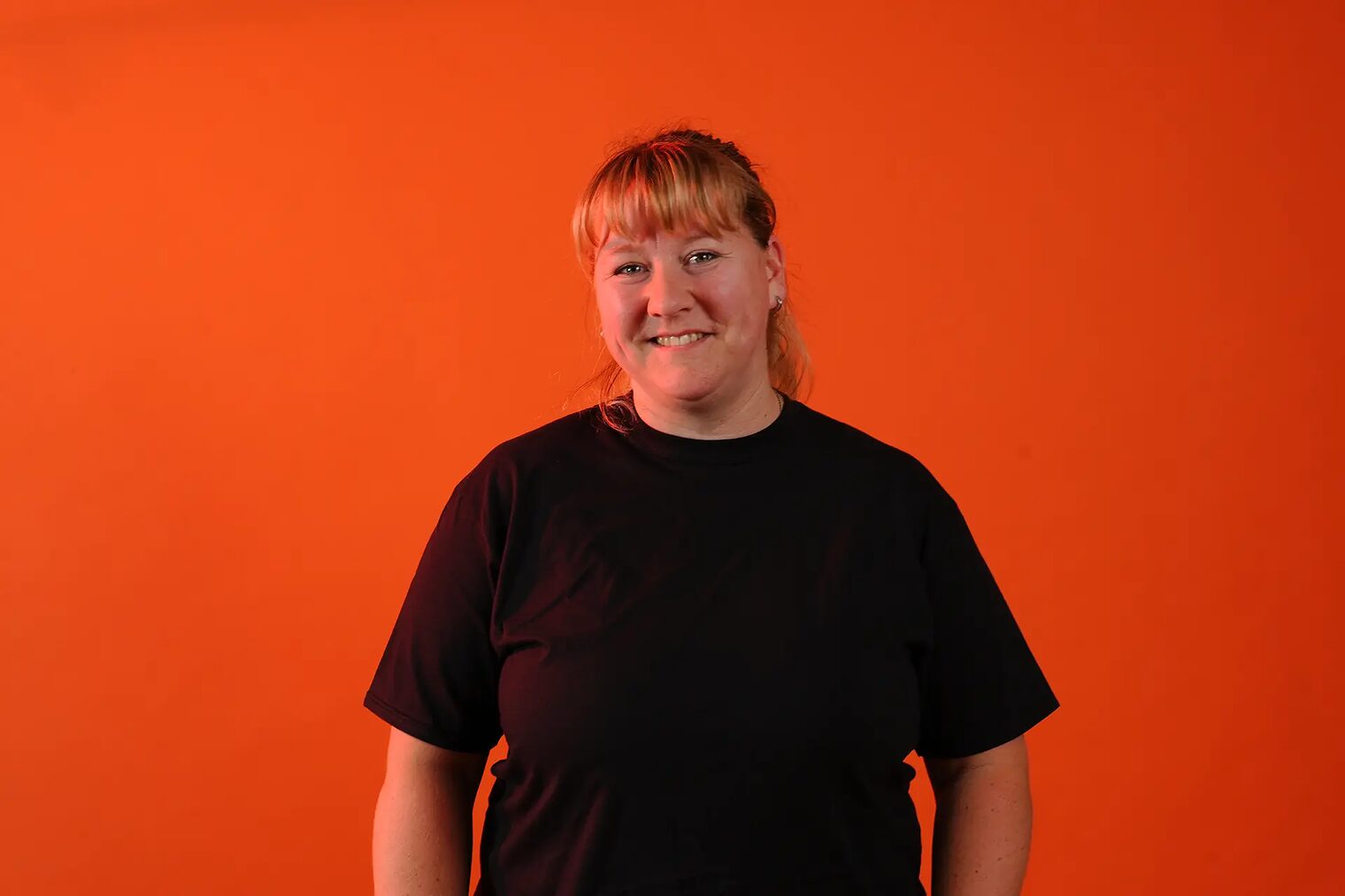 Portrait einer Dozentin, vor orangenem Hintergrund. Frau Nitzsche, Lackierermeisterin.