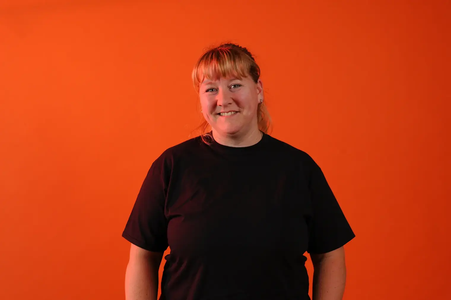 Portrait einer Dozentin, vor orangenem Hintergrund. Frau Nitzsche, Lackierermeisterin.