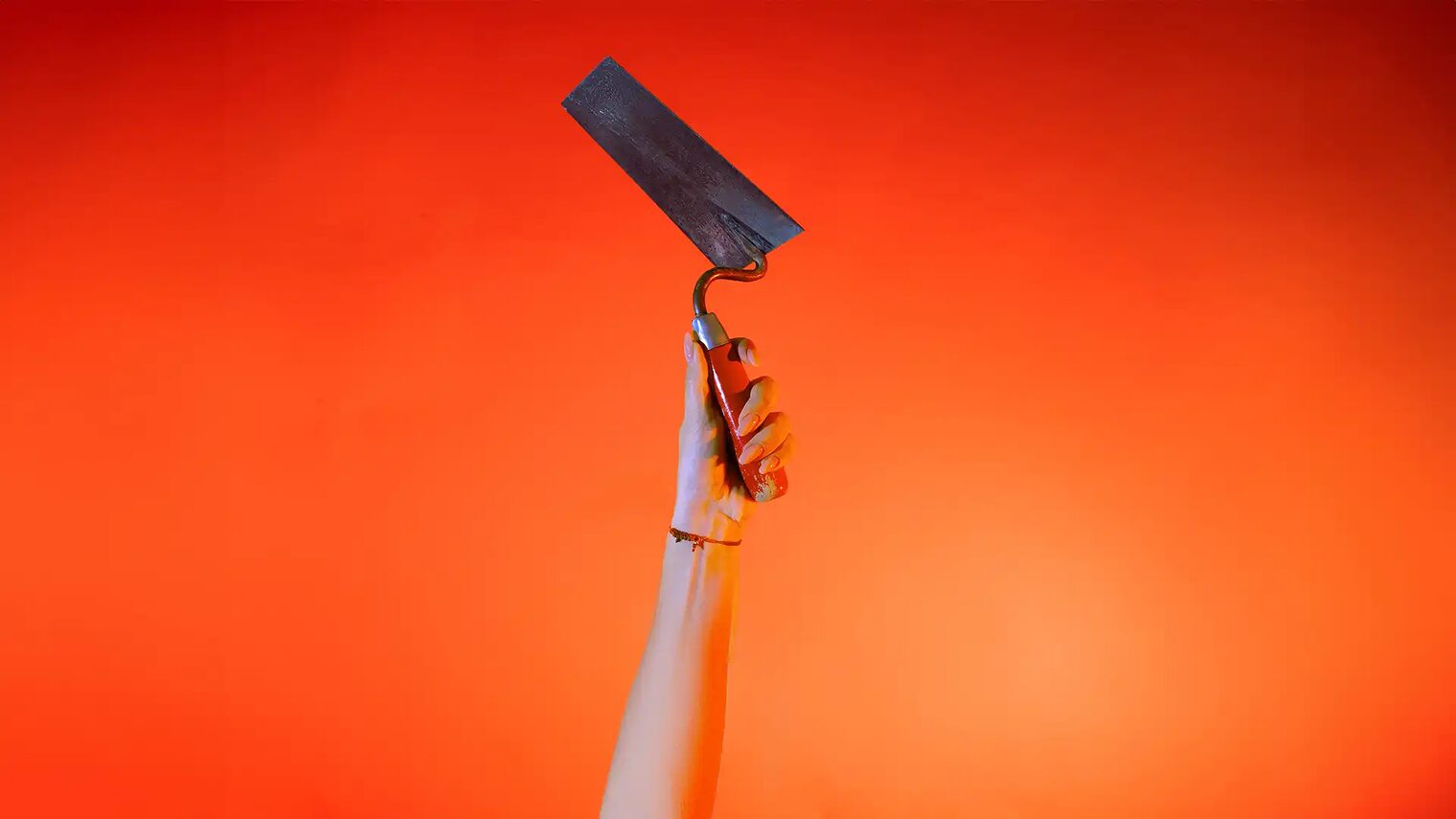 Ein Hand streckt vor orangenem Hintergrund eine Maurerkelle senkrecht nach oben.
