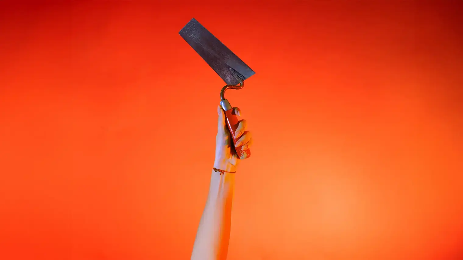 Ein Hand streckt vor orangenem Hintergrund eine Maurerkelle senkrecht nach oben.