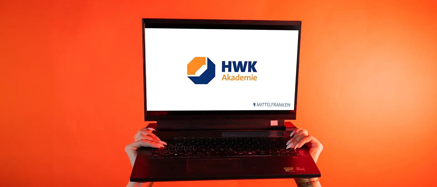 Zwei Hände heben einen Laptop in die Luft. Der Bildschirm ist weiß und mittig liegt das Logo Akademie.